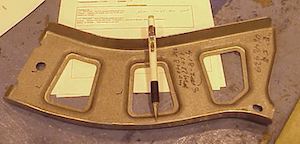 Form steel Autopart with pen on top indicating scale of part.